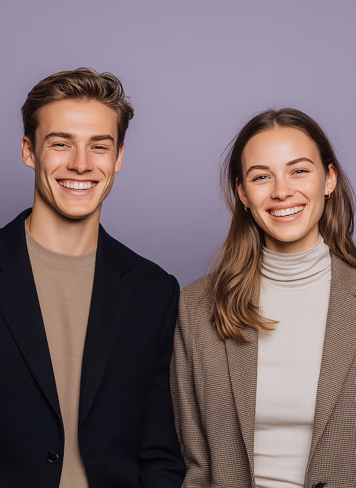 Young man and woman standing side by side, smiling against a plain purple background.